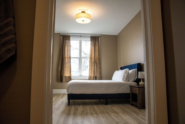 A bedroom with a bed, a nightstand, a lamp, and a window with curtains.