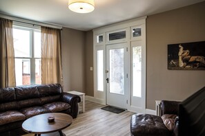 A living room with a leather sofa, a coffee table, a door with glass panels, and a painting on the wall.