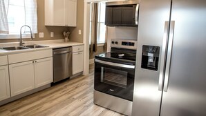 A modern kitchen with stainless steel appliances, white cabinetry, and a wooden floor.