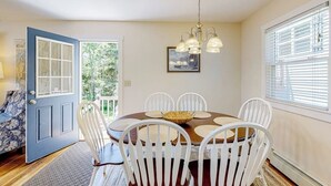 A dining area with a round table, white chairs, a chandelier, and a door leading outside. - Barrett's Watch Main House- Oceanfront on Lobster Cove with deck & shared firepit - walk to town (Boothbay Harbor)