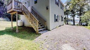 A two-story house with a wooden deck and a staircase leading to the second floor. - Barrett's Watch Main House- Oceanfront on Lobster Cove with deck & shared firepit - walk to town (Boothbay Harbor)