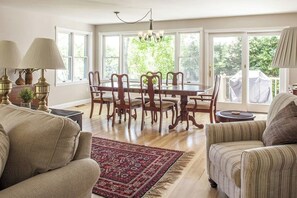 A dining area with a table and chairs, a chandelier, and a view through large windows.