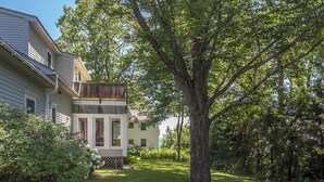 A two-story house with a visible balcony, surrounded by lush greenery and a large tree. - Great home with water view - one house from harbor - washer/dryer & dog-friendly (Camden)
