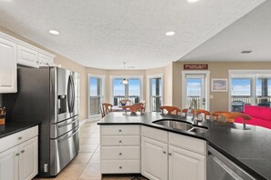 Una cocina con armarios blancos, un refrigerador de acero inoxidable, una encimera negra y vistas al balcón.