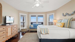Un dormitorio con cama, televisor, ventilador de techo y vistas al cielo a través de ventanas.