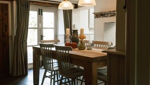 Un comedor con una mesa de madera, sillas, una araña y una ventana con cortinas.