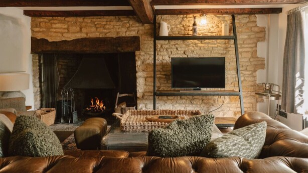 Una sala de estar acogedora con chimenea de piedra, sofá de cuero y televisor montado.