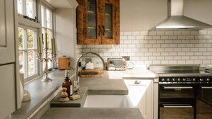 Una cocina con salpicadero de azulejos blancos, un armario de madera, una estufa y una ventana con vistas.