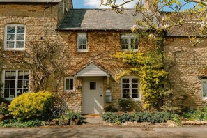 A stone house with a central door, windows, and a small porch. - Charming Cotswold Cottage with Garden Annexe (Little Compton)