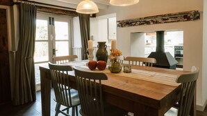 Un comedor con mesa de madera, sillas, un florero con flores, velas y decoración rústica en la pared.
