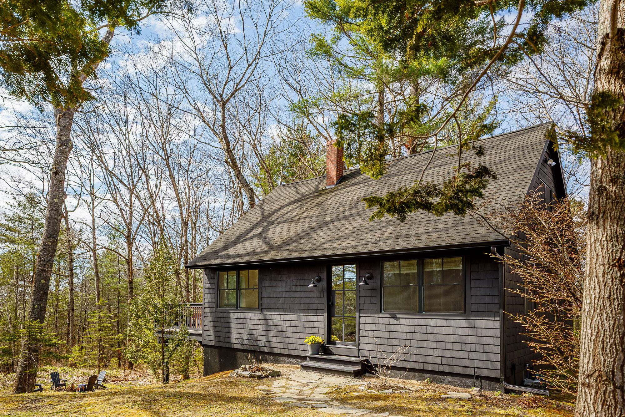 A cabin with a dark exterior, large windows, and a chimney.