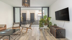 Een moderne woonkamer met een houten vloer, een zwart aan de muur bevestigd televisietoestel, een bank, een stoel en een potplant.