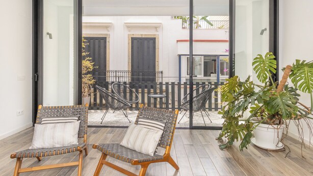 Een balkon met twee rieten stoelen, een bloempot en uitzicht op een gebouw met luiken.