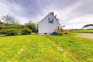 A single-story house with a sloped roof, a front porch, and a well-maintained lawn. - Serene home with a deck, grill, firepit, board games, washer/dryer, & mtn views (Lamoine)