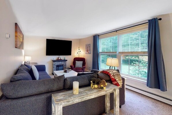 A living room with a sofa, a red armchair, a fireplace, and a large window with curtains.