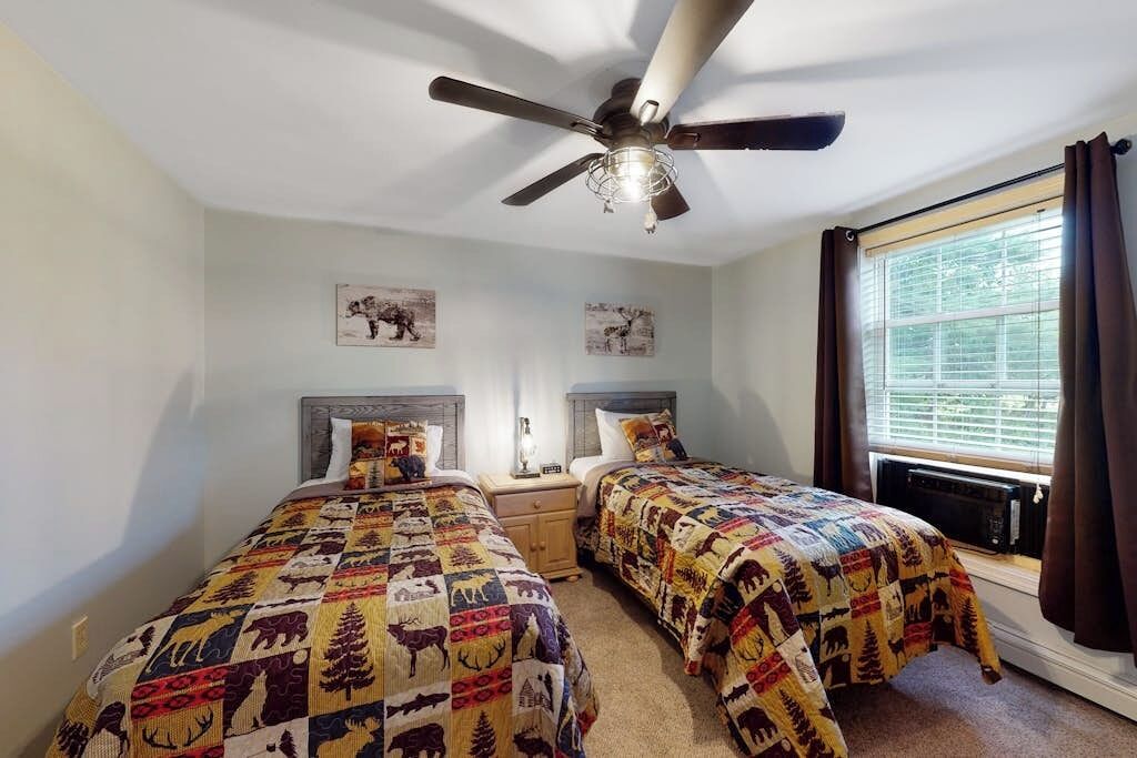 A bedroom with two beds, a ceiling fan, and a window with curtains.
