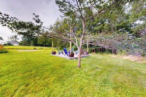 A grassy outdoor area with a tree, blue chairs, and a concrete structure. - Serene home with a deck, grill, firepit, board games, washer/dryer, & mtn views (Lamoine)