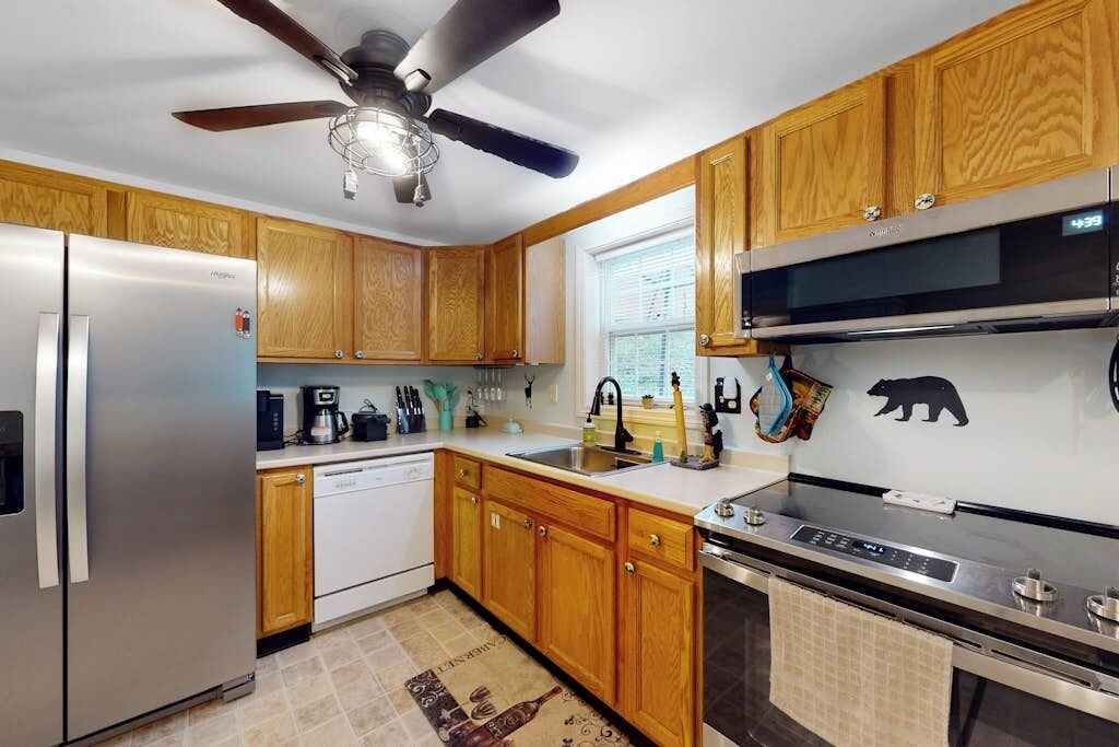 A kitchen with wooden cabinets, a stainless steel refrigerator, a dishwasher, a stove, and a ceiling fan.