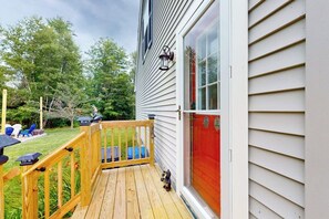 A wooden deck with a railing, a red door, and a window with a light fixture.