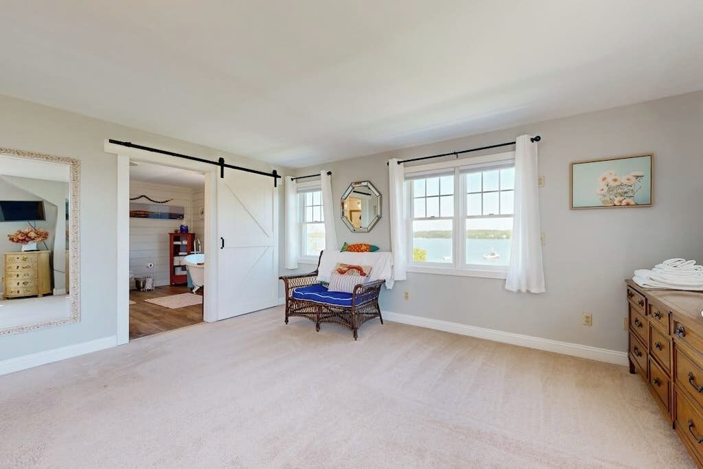 A spacious room with a large window, a wicker chair, a wooden dresser, and a mirror on the wall.