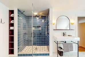 Une salle de bain avec une douche à parois de verre, un lavabo blanc et un miroir agrémenté d’appliques murales.