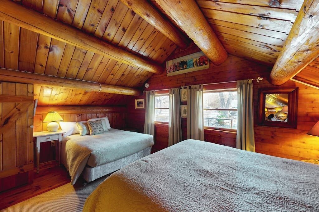 Une chambre dans une cabane en bois, avec un lit, une table de chevet et une fenêtre avec des rideaux.