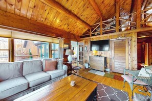 A cabin interior with a wooden ceiling, a sofa, a table, and a view through the windows. - Riverfront retreat with a furnished deck, washer/dryer & fast WiFi (Boothbay)