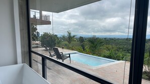 A modern bathroom with a bathtub, a view of a swimming pool, and a balcony overlooking lush greenery. - Villa with infinity pool and 180° views Filandia (Filandia)