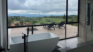 A modern bathroom with a large bathtub, a glass shower enclosure, and a view of a green landscape through large windows. - Villa with infinity pool and 180° views Filandia (Filandia)