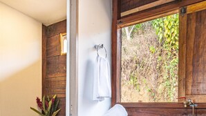 A bathroom with a wooden vanity, a toilet, a window with a view of greenery, and two woven baskets. - Nebula · Mountain Ecolodge near Minca (Vista Nieves, Santa Marta)