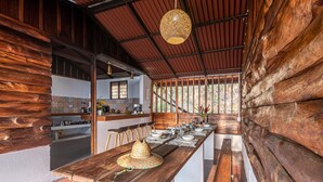 A long wooden dining table set with white plates, glasses, and a straw hat. - Nebula · Mountain Ecolodge near Minca (Vista Nieves, Santa Marta)