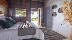 A bedroom with a bed, a view through an open door, a wall with decorative plates, and a hanging plant. - Nebula · Mountain Ecolodge near Minca (Vista Nieves, Santa Marta)