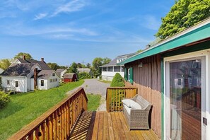 Eine Holzterrasse mit einer Korbsitzgruppe, einer Glastür und Blick auf benachbarte Häuser.