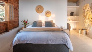 Ein Schlafzimmer mit einem Bett, zwei Wandregalen mit Hüten, einem Nachttisch mit Blumenvase und einer großen Pflanze.