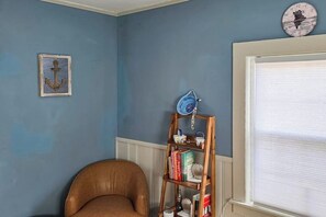 A room with a blue wall, a wooden chair, a bookshelf with books, a decorative anchor, and a clock on the wall.