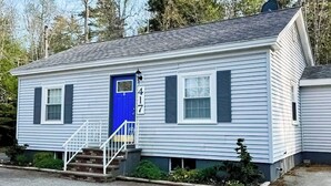 Ein eingeschossiges Haus mit blauer Tür, weißer Fassade und einer kleinen Veranda mit Stufen.