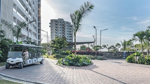 A paved walkway with a golf cart, surrounded by lush greenery and tall buildings. - Panoramic Loft with Balcony at Santa Marina, 21st (Santa marta)