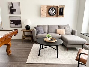 A living room with a pool table, a sofa, a coffee table, and a dartboard. - Cozy Home with HotTub, Patio, Grill & Park Views (Gilbert)