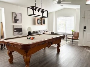 A pool table in a room with a ceiling fan, a dartboard, and a clock on the wall. - Cozy Home with HotTub, Patio, Grill & Park Views (Gilbert)