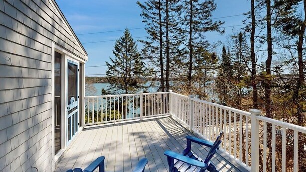A wooden deck with chairs, a railing, and a view of trees and water.