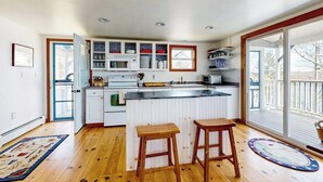 A kitchen with a central island, wooden stools, and a large sliding glass door to the outdoors.