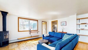 A living room with a blue sofa, a black wood-burning stove, a window, and a door leading to another room.