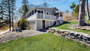 A two-story house with a balcony, stone retaining wall, and a lawn.