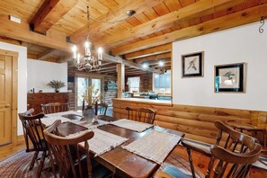 A wooden dining room with a chandelier, wooden walls, and framed artwork.