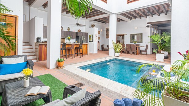 A modern indoor pool area with a bar, seating, and a kitchen in the background. - Room in Colonial House with Pool and Rooftop (Santa Marta)