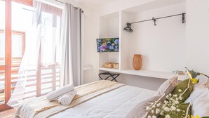 A bedroom with a bed, a television, a shelf with items, and a view through a window. - Room in Colonial House with Pool and Rooftop (Santa Marta)