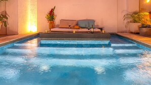 A poolside area with a sofa, cushions, a vase with flowers, and a bottle of wine. - Room in Colonial House with Pool and Rooftop (Santa Marta)