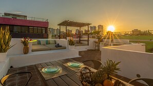 A rooftop terrace with a seating area, a pergola, and a view of the sunset over a cityscape. - Room in Colonial House with Pool and Rooftop (Santa Marta)