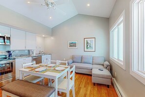 A modern kitchen with white cabinets, a dining table with chairs, a gray sofa, and a small ottoman. - Waterfront, dog-friendly suite with Broad Cove access, firepit & sunrise view (Waldoboro)