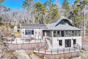 A modern cabin with a deck, large windows, and solar panels.